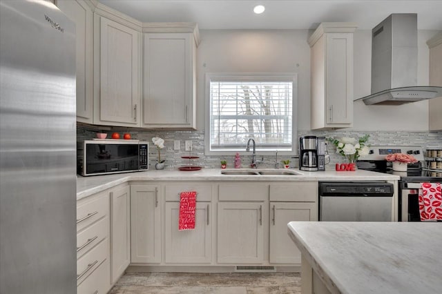 kitchen with wall chimney range hood, sink, appliances with stainless steel finishes, backsplash, and light wood-type flooring