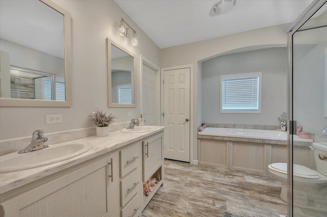 bathroom featuring wood-type flooring, a tub, vanity, toilet, and a healthy amount of sunlight