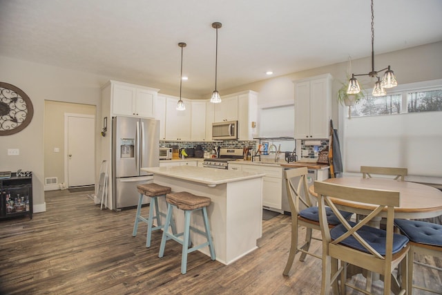 kitchen with white cabinets, decorative light fixtures, a kitchen island, and appliances with stainless steel finishes