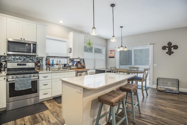 kitchen with a center island, white cabinets, sink, decorative light fixtures, and stainless steel appliances