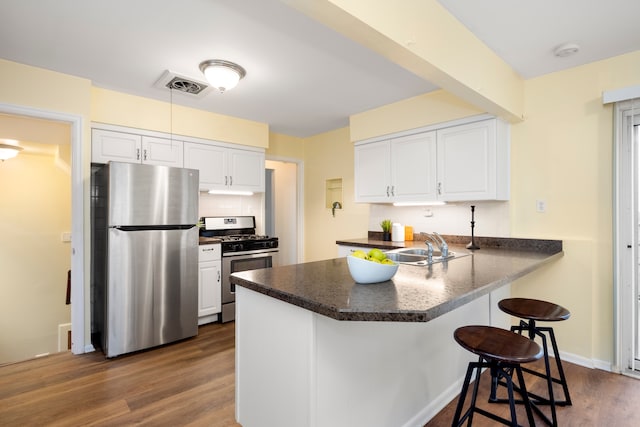 kitchen featuring a breakfast bar, hardwood / wood-style floors, white cabinets, kitchen peninsula, and stainless steel appliances