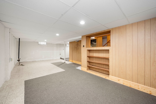 basement featuring built in shelves, a paneled ceiling, and wood walls