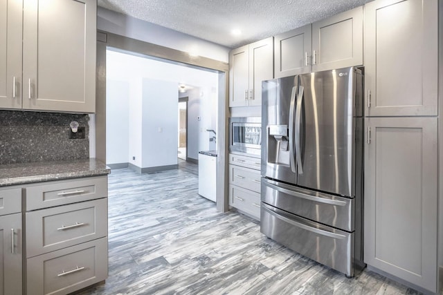 kitchen featuring light hardwood / wood-style floors, a textured ceiling, appliances with stainless steel finishes, tasteful backsplash, and gray cabinetry