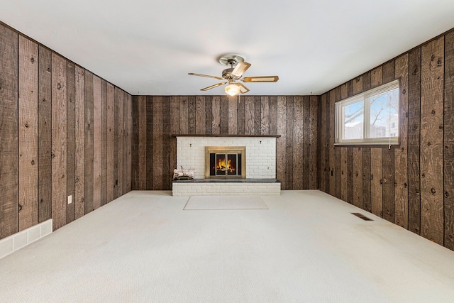 unfurnished living room featuring a brick fireplace, carpet floors, ceiling fan, and wood walls