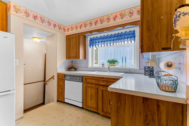 kitchen with light floors, light countertops, brown cabinetry, a sink, and white appliances