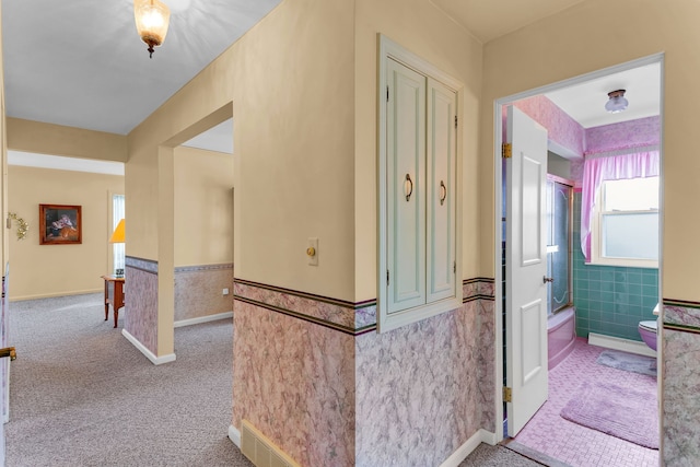 hallway with wainscoting, carpet flooring, and tile walls