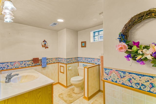 bathroom with visible vents, wainscoting, toilet, tile patterned flooring, and tile walls