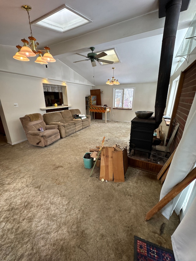 carpeted living room featuring vaulted ceiling with skylight, ceiling fan with notable chandelier, and a wood stove