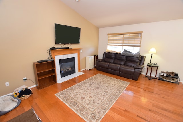 living room featuring lofted ceiling, radiator heating unit, hardwood / wood-style floors, and a tile fireplace