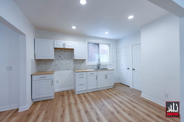 kitchen with white cabinets, light hardwood / wood-style floors, sink, and backsplash