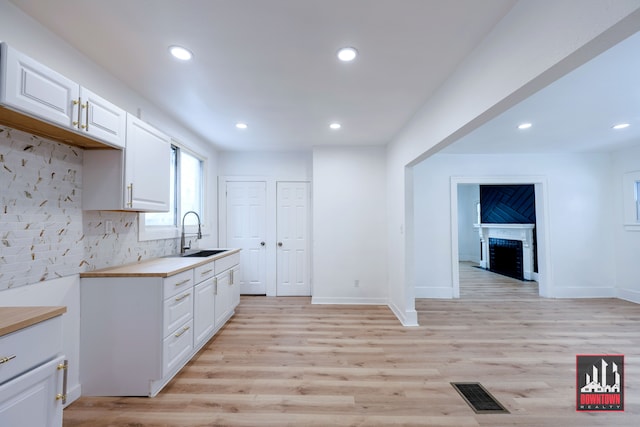 kitchen featuring white cabinetry, sink, backsplash, and light wood-type flooring