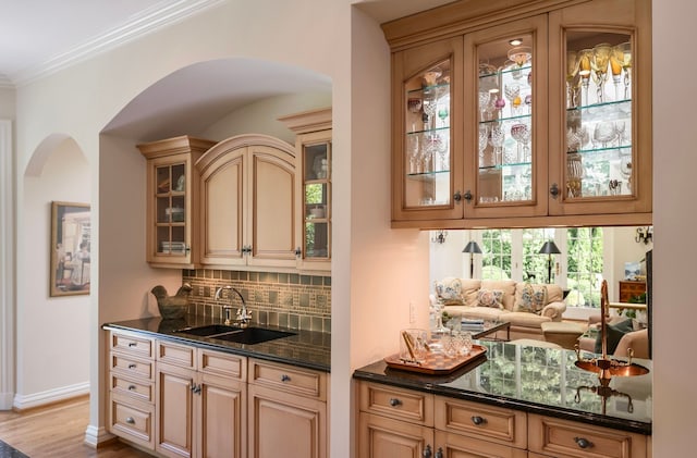 bar featuring sink, crown molding, tasteful backsplash, dark stone counters, and light wood-type flooring