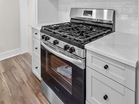 kitchen featuring white cabinetry, stainless steel gas range oven, decorative backsplash, and light hardwood / wood-style flooring