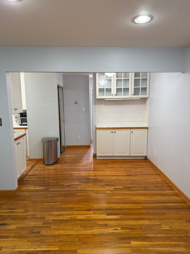 interior space with tasteful backsplash, wood-type flooring, and white cabinets