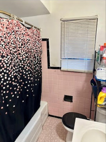 bathroom with tile walls, tile patterned floors, toilet, and shower / bath combo with shower curtain