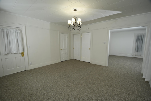 spare room featuring crown molding, a chandelier, and dark colored carpet