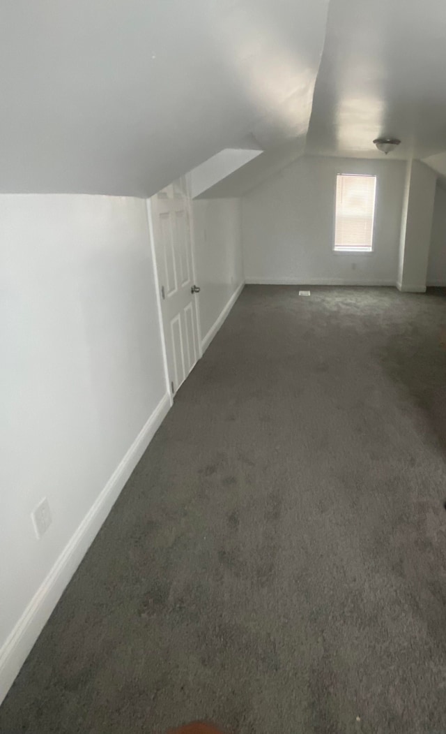 additional living space featuring dark colored carpet and vaulted ceiling