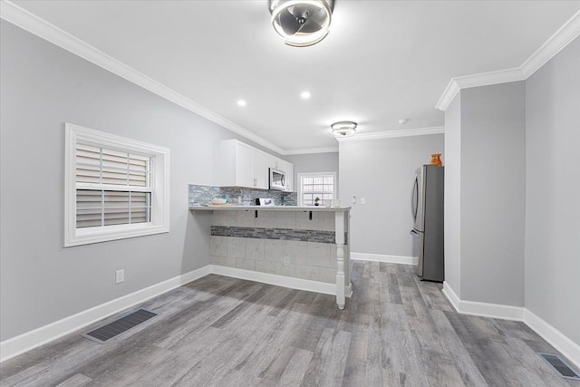 kitchen with white cabinetry, stainless steel appliances, decorative backsplash, kitchen peninsula, and a breakfast bar