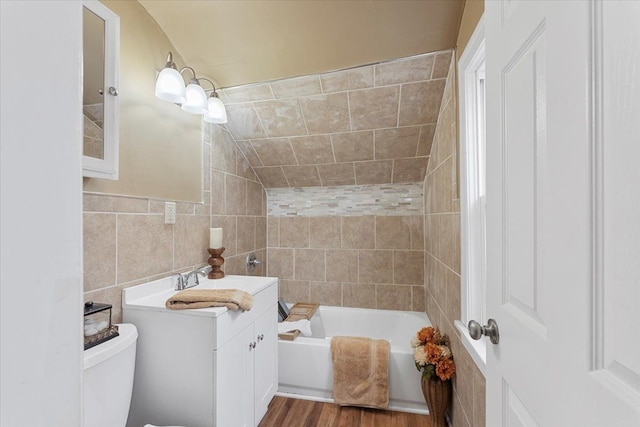 full bathroom with tiled shower / bath combo, vanity, toilet, vaulted ceiling, and hardwood / wood-style flooring