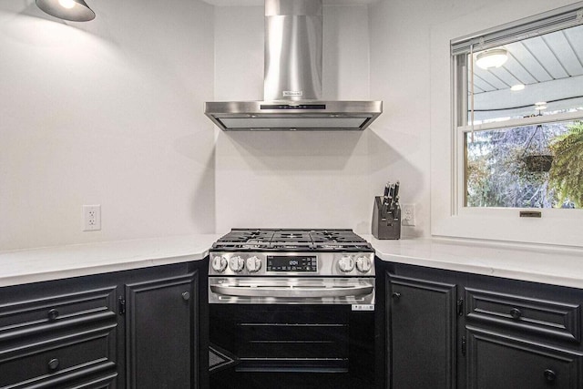 kitchen featuring light stone countertops, stainless steel range with gas cooktop, and wall chimney range hood