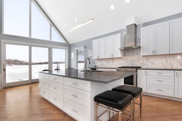 kitchen featuring a breakfast bar, white cabinetry, sink, gas stove, and wall chimney exhaust hood