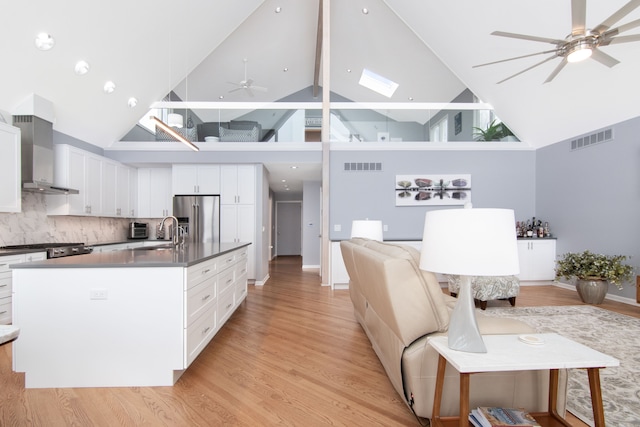 kitchen with wall chimney exhaust hood, sink, high end refrigerator, ceiling fan, and white cabinets