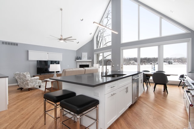 kitchen with a kitchen bar, sink, white cabinetry, dishwasher, and a kitchen island with sink