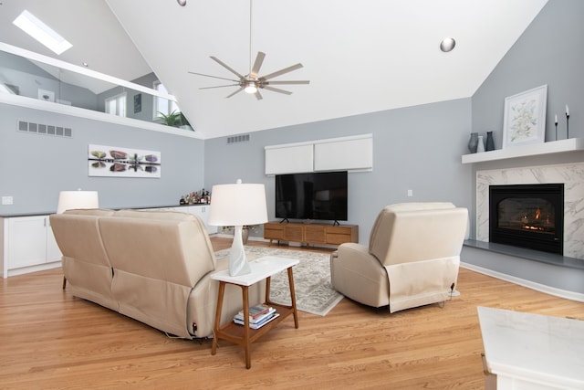 living room with a premium fireplace, high vaulted ceiling, ceiling fan, and light hardwood / wood-style flooring