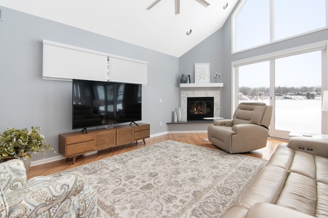 living room featuring ceiling fan, a fireplace, high vaulted ceiling, and light hardwood / wood-style flooring