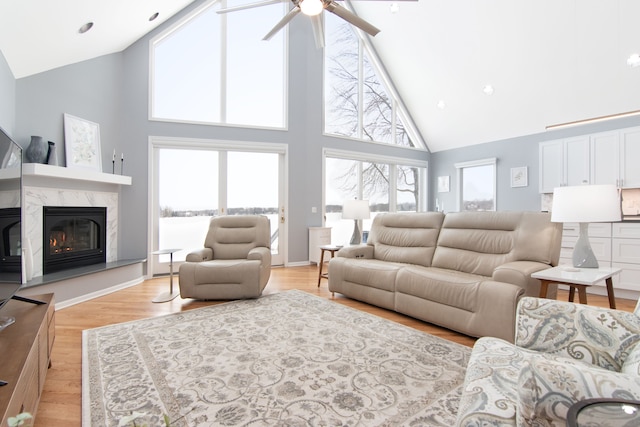 living room with a fireplace, high vaulted ceiling, ceiling fan, and light wood-type flooring