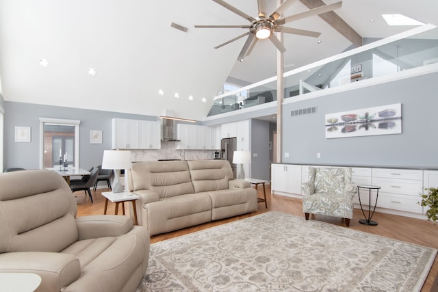 living room with ceiling fan, beam ceiling, a skylight, high vaulted ceiling, and light wood-type flooring