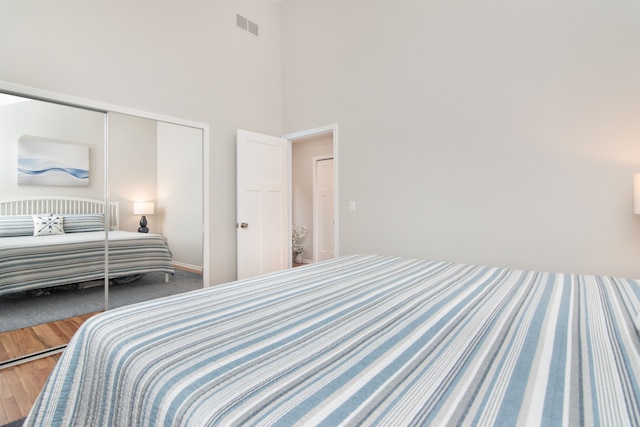 bedroom with a towering ceiling, hardwood / wood-style floors, and a closet