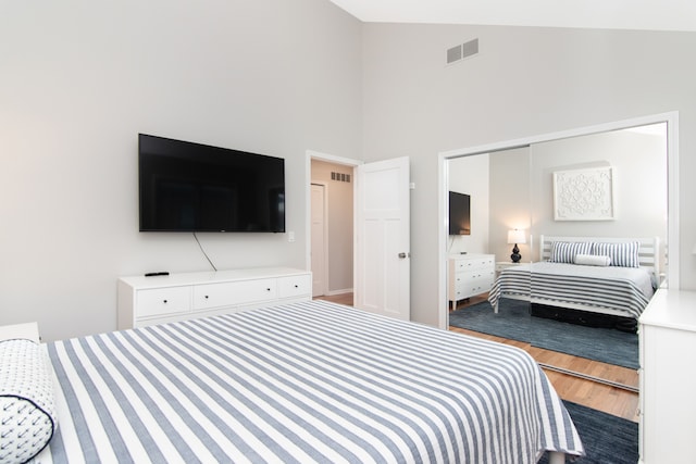 bedroom featuring wood-type flooring, high vaulted ceiling, and a closet