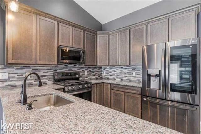 kitchen featuring appliances with stainless steel finishes, sink, tasteful backsplash, light stone counters, and lofted ceiling