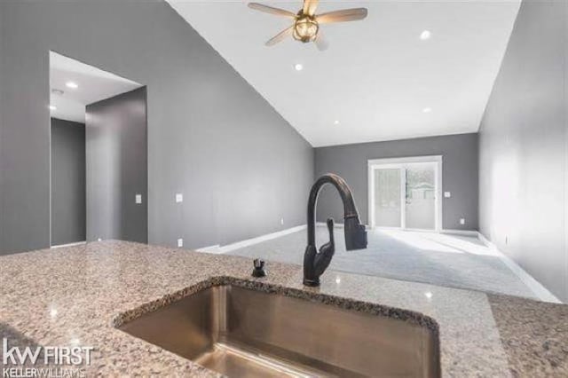 kitchen with ceiling fan, sink, lofted ceiling, and light stone countertops