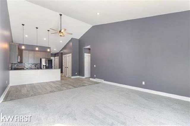 unfurnished living room with light colored carpet, high vaulted ceiling, and ceiling fan