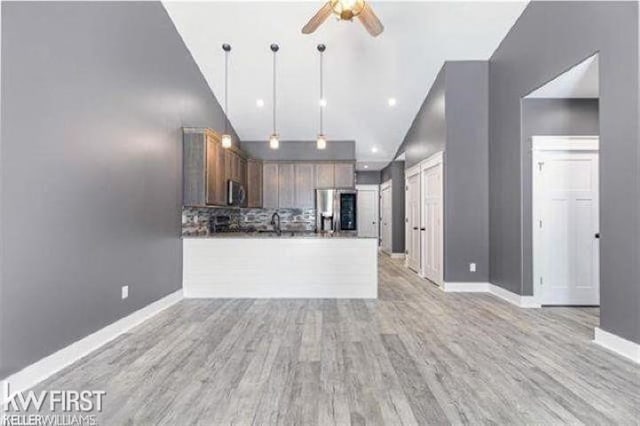 kitchen with light hardwood / wood-style floors, appliances with stainless steel finishes, kitchen peninsula, pendant lighting, and backsplash