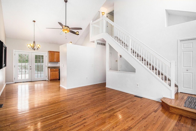 unfurnished living room featuring ceiling fan with notable chandelier, high vaulted ceiling, french doors, and light wood-type flooring