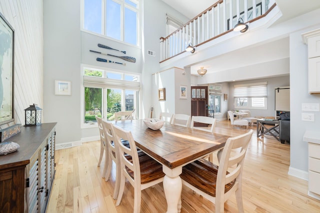 dining area with light wood-type flooring, a towering ceiling, and a healthy amount of sunlight