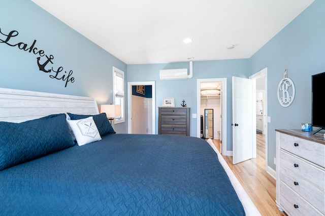 bedroom with a walk in closet, a wall mounted air conditioner, and light hardwood / wood-style flooring