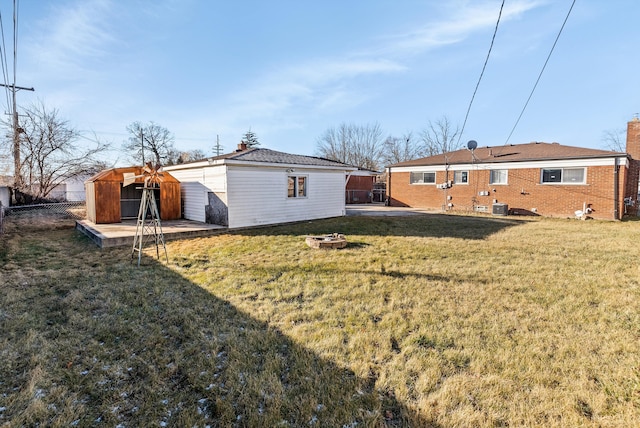 rear view of house featuring cooling unit, a storage shed, a fire pit, and a lawn