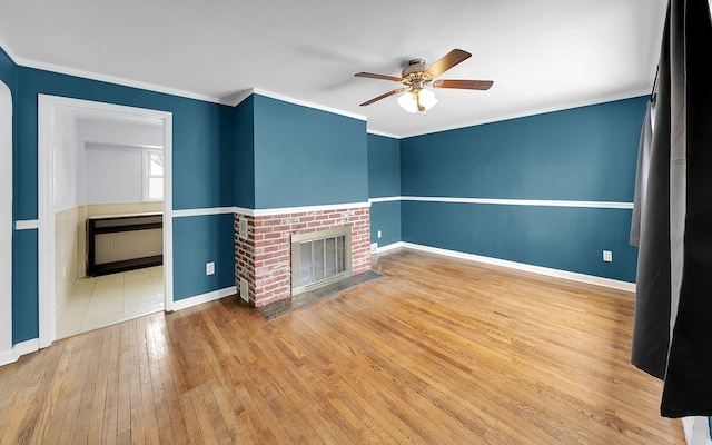 unfurnished living room with a fireplace, wood-type flooring, ornamental molding, ceiling fan, and baseboards