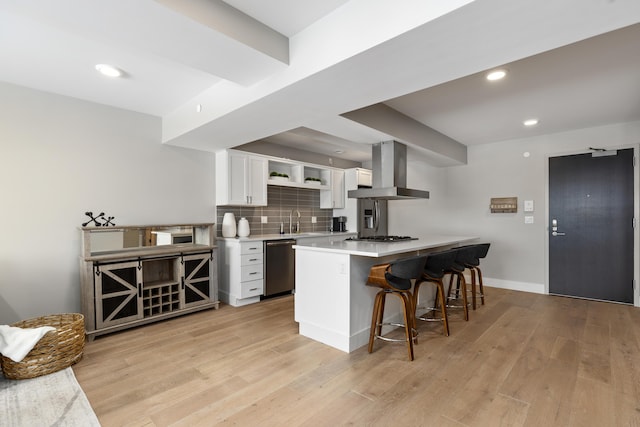 kitchen with appliances with stainless steel finishes, range hood, white cabinets, kitchen peninsula, and a breakfast bar area