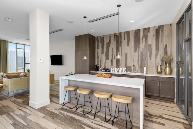 kitchen featuring a kitchen breakfast bar, hanging light fixtures, sink, a center island, and wood walls