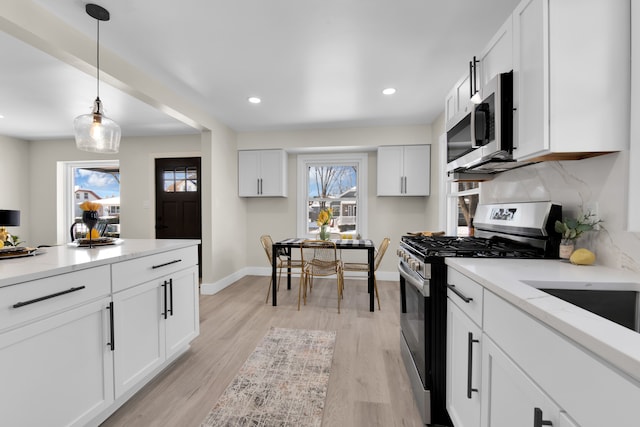 kitchen featuring light hardwood / wood-style flooring, appliances with stainless steel finishes, pendant lighting, decorative backsplash, and white cabinets