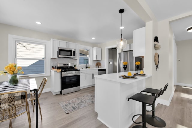 kitchen featuring pendant lighting, kitchen peninsula, white cabinets, and appliances with stainless steel finishes