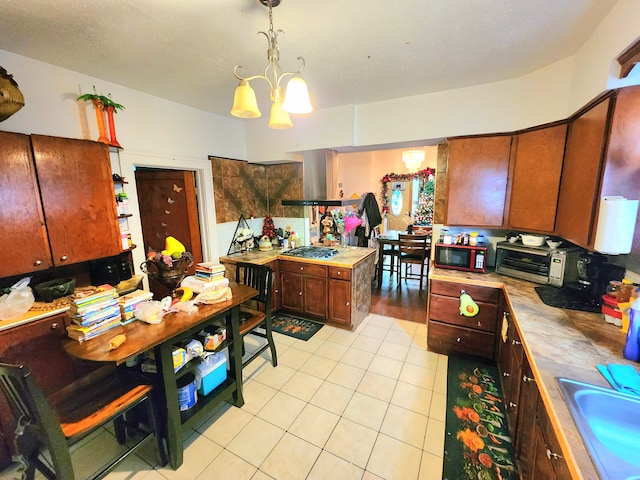 kitchen featuring sink, stainless steel gas cooktop, hanging light fixtures, light tile patterned floors, and wall chimney range hood