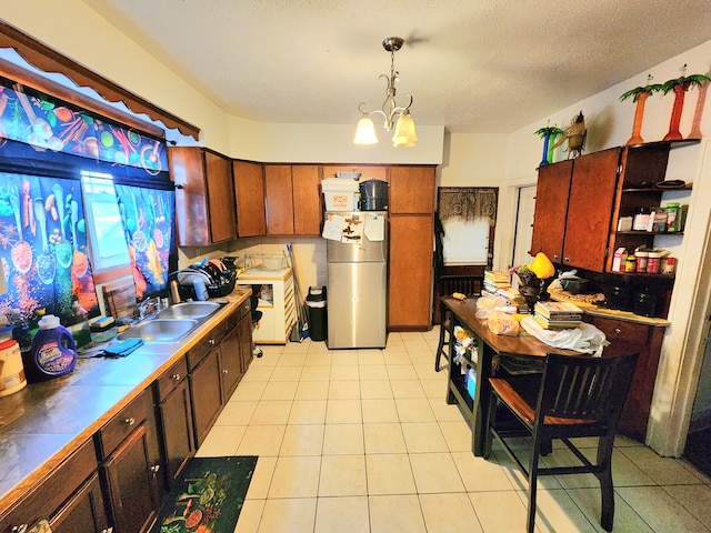 kitchen featuring pendant lighting, sink, stainless steel fridge, an inviting chandelier, and a textured ceiling