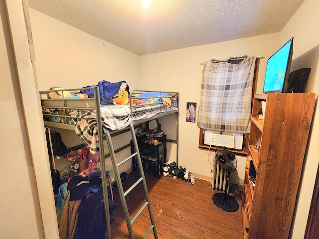 bedroom featuring cooling unit, wood-type flooring, and a textured ceiling