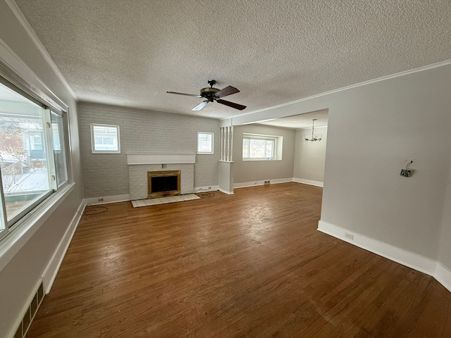 unfurnished living room with ceiling fan with notable chandelier, a textured ceiling, brick wall, dark hardwood / wood-style flooring, and a fireplace